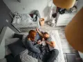Rodzice bawią się z dzieckiem na łóżku w pokoju, który jest jednocześnie sypialnią i pokojem dziecka. Obok łóżeczko dziecięce.