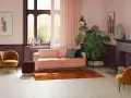 Przytulny salon z kanapą w kolorze pudrowy róż, aksamitnym fotelem i dużą rośliną.
