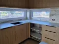 Nowoczesna kuchnia z drewnianymi frontami i marmurowym blatem. Okna z widokiem na ogród. Zobacz, jak połączyć parapet z blatem kuchennym.
