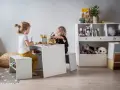 Dwie dziewczynki bawią się przy stoliku, tworząc przytulny kącik zabaw dla dziecka w salonie. Na półkach stoją pluszaki i książki.