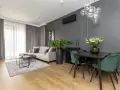 Nowoczesny salon z sofą w odcieniu beżu, dywanem w barwie szarej i zielonymi krzesłami przy czarnym stole.