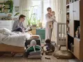Wspólny pokój rodziców z dzieckiem. Ojciec pracuje przy laptopie, matka tuli niemowlę, starsze dziecko bawi się klockami.