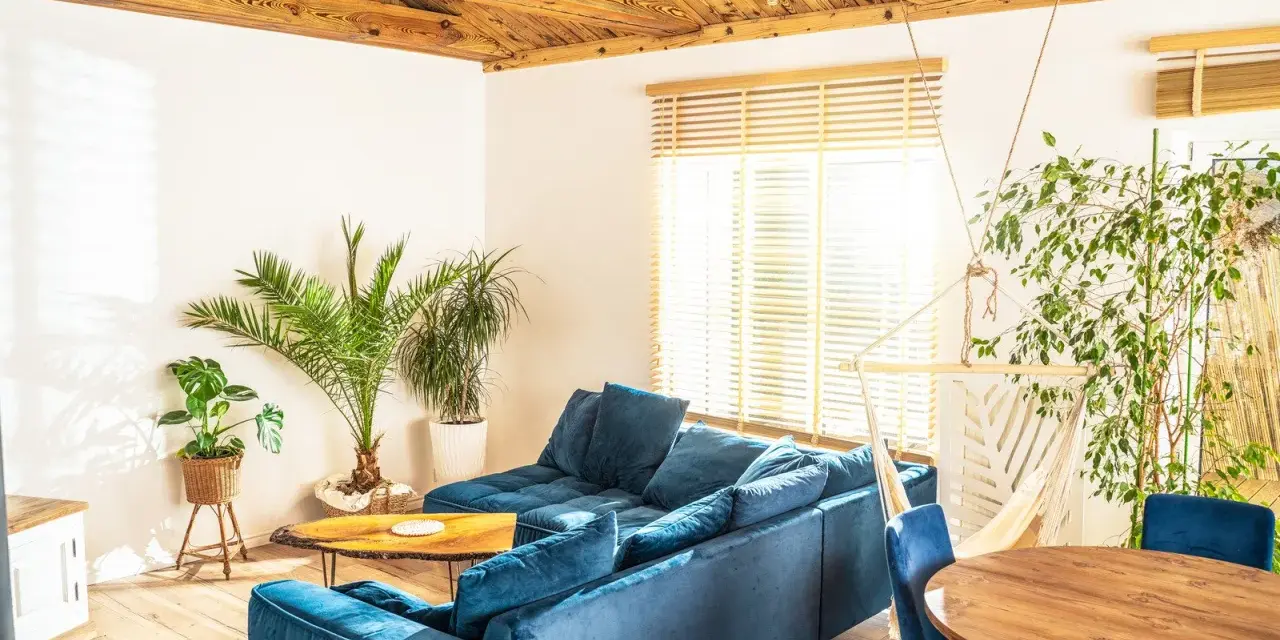 Przytulny salon w stylu włoskim z wygodną, granatową kanapą, drewnianym stołem i bujnym zielonym otoczeniem.