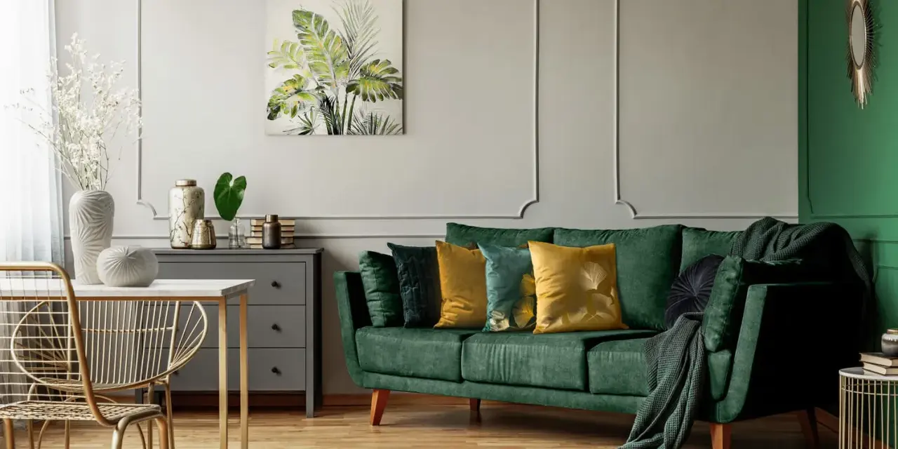 Jak rozjaśnić salon z ciemnymi meblami? Zielona sofa, złote akcenty i jasne dodatki dodają lekkości.