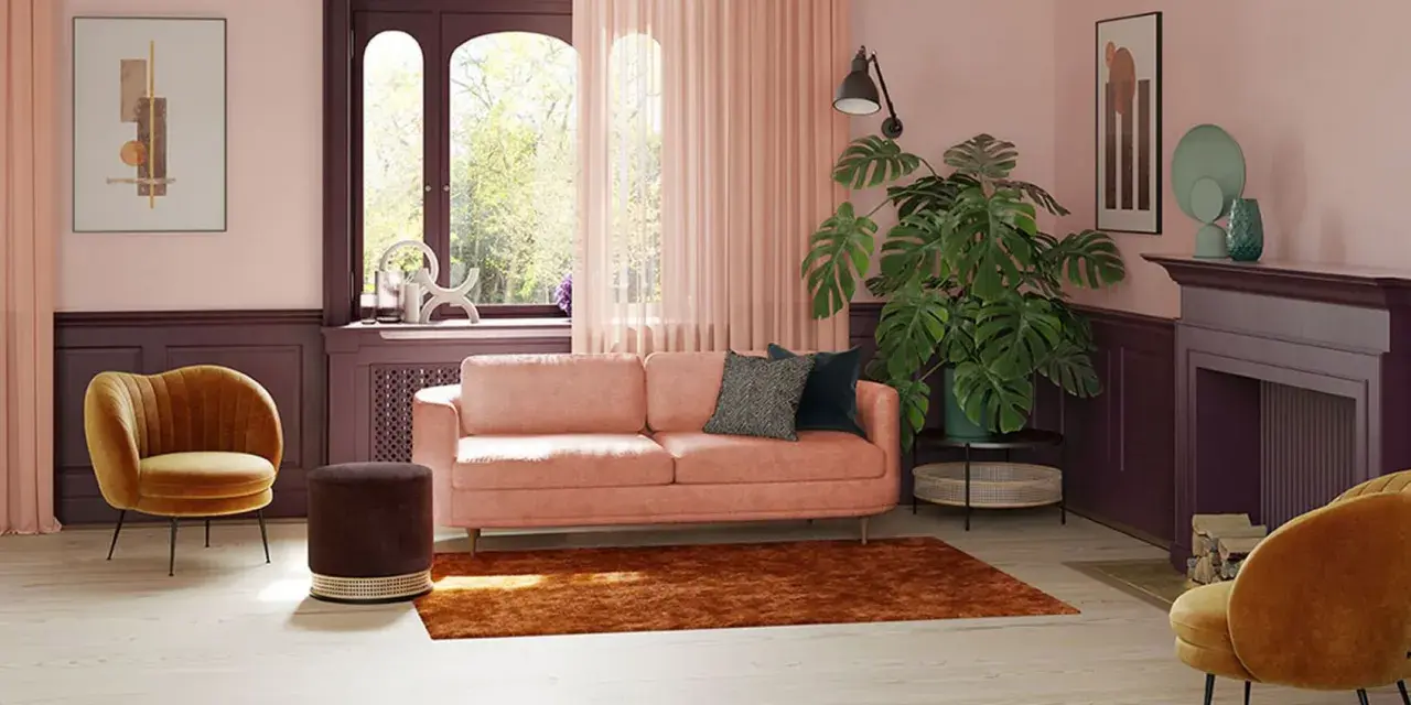 Przytulny salon z kanapą w kolorze pudrowy róż, aksamitnym fotelem i dużą rośliną.