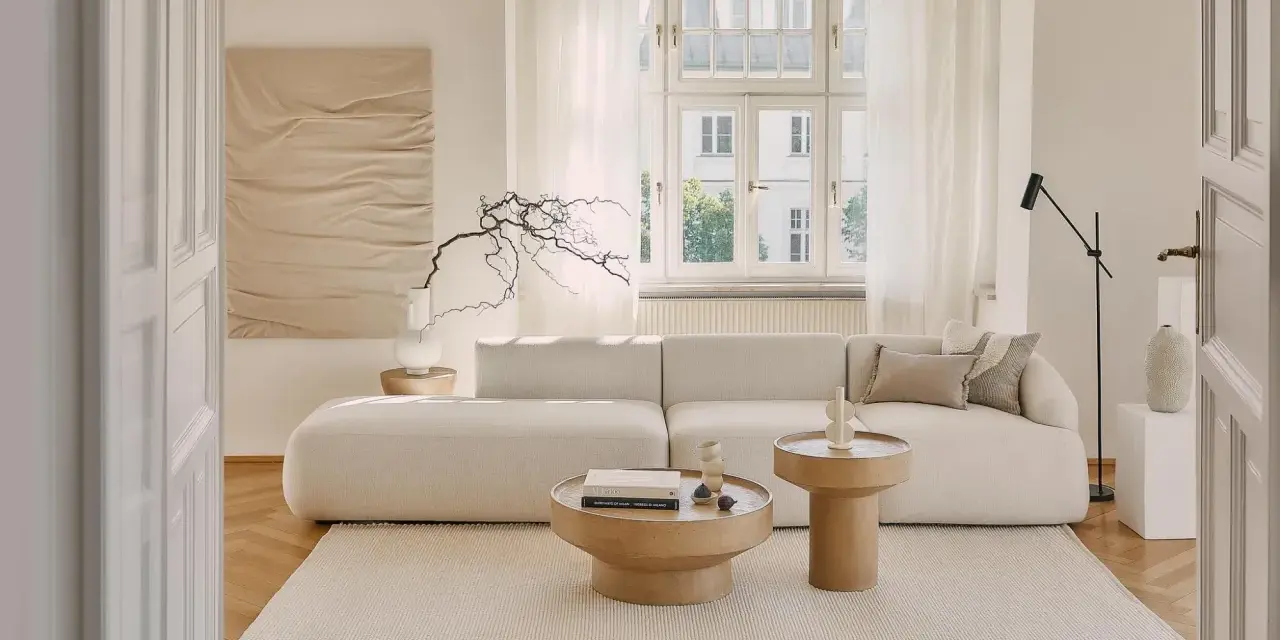 Jasny salon z sofą i stolikami kawowymi. Białe meble na białej ścianie tworzą minimalistyczną, spokojną przestrzeń.