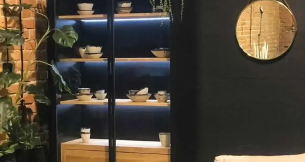 Elegancka witryna w salonie z podświetlanymi półkami, na których stoją misy i filiżanki. Idealna inspiracja, co wstawić do witryny w salonie.