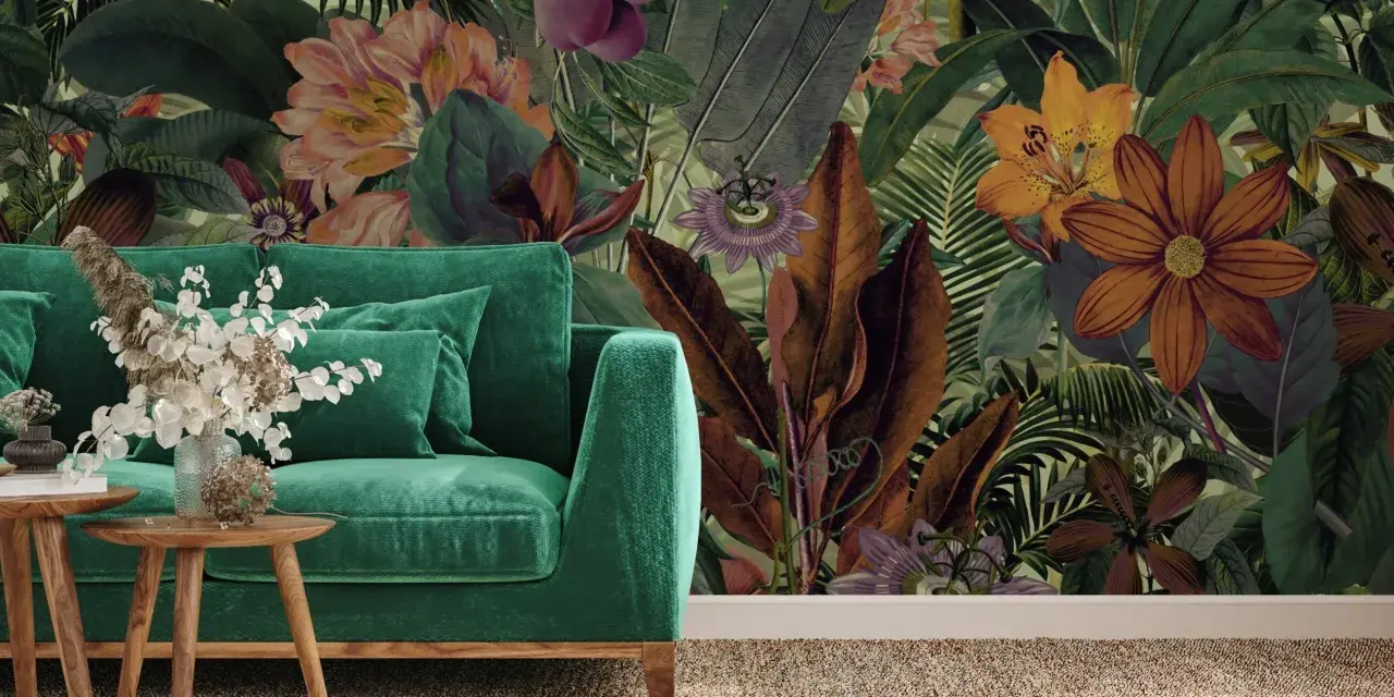 Aksamitna sofa w odcieniach zieleni, obok niej drewniane stoliki z bukietem. W tle bujna, tropikalna tapeta z kwiatami i liśćmi.