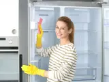 Kobieta w żółtych rękawiczkach czyści wnętrze lodówki różową gąbką. Pokazuje, jak myć lodówkę, by była lśniąca.