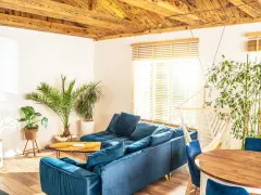 Przytulny salon w stylu włoskim z wygodną, granatową kanapą, drewnianym stołem i bujnym zielonym otoczeniem.