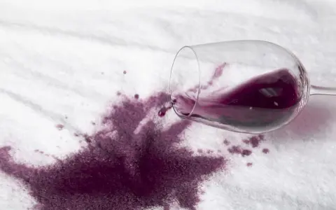 Rozlane czerwone wino na białym materiale. Dowiedz się, jak usunąć plamę z wina, zanim zaschnie.