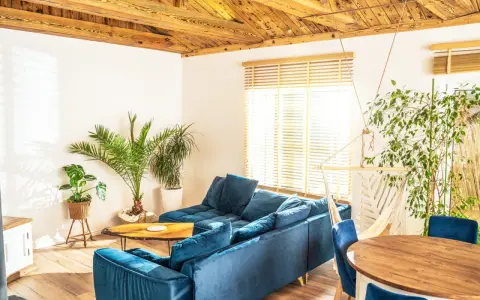 Przytulny salon w stylu włoskim z wygodną, granatową kanapą, drewnianym stołem i bujnym zielonym otoczeniem.