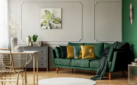 Jak rozjaśnić salon z ciemnymi meblami? Zielona sofa, złote akcenty i jasne dodatki dodają lekkości.