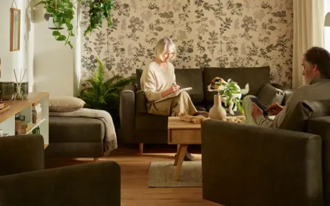Przytulny salon, gdzie starsza pani pisze w notatniku, a pan czyta na tablecie. Idealne miejsce, by pomyśleć, jak urządzić pokój dla babci.