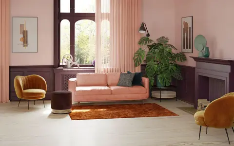 Przytulny salon z kanapą w kolorze pudrowy róż, aksamitnym fotelem i dużą rośliną.