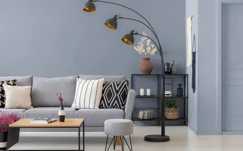 Nowoczesny salon z szarą kanapą i stolikiem. Lampę łukową w kolorze grafitowym oświetla złote wnętrze kloszy.