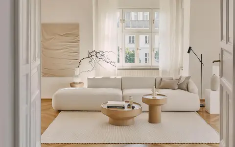 Jasny salon z sofą i stolikami kawowymi. Białe meble na białej ścianie tworzą minimalistyczną, spokojną przestrzeń.