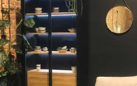 Elegancka witryna w salonie z podświetlanymi półkami, na których stoją misy i filiżanki. Idealna inspiracja, co wstawić do witryny w salonie.