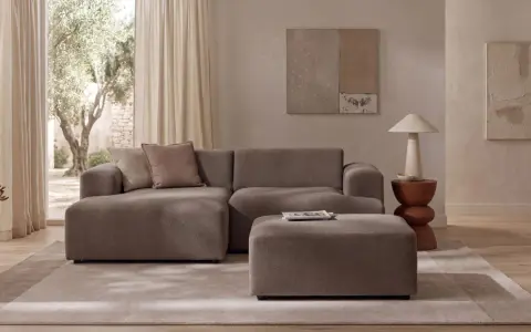 Wygodna sofa i puf w kolorze greige jaki to kolor, idealnie komponują się z jasnym wnętrzem i widokiem na drzewa.