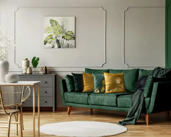 Jak rozjaśnić salon z ciemnymi meblami? Zielona sofa, złote akcenty i jasne dodatki dodają lekkości.
