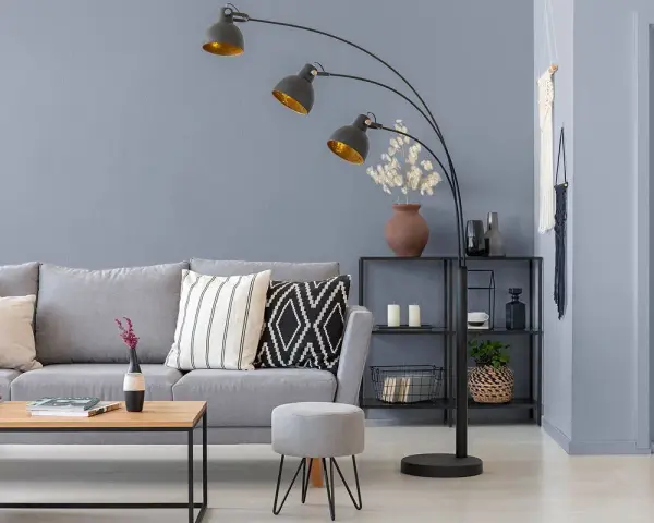 Nowoczesny salon z szarą kanapą i stolikiem. Lampę łukową w kolorze grafitowym oświetla złote wnętrze kloszy.