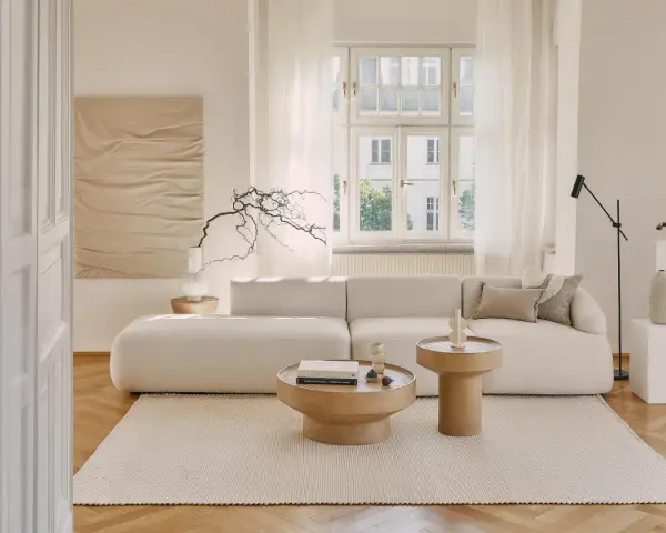 Jasny salon z sofą i stolikami kawowymi. Białe meble na białej ścianie tworzą minimalistyczną, spokojną przestrzeń.