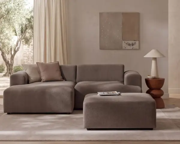 Wygodna sofa i puf w kolorze greige jaki to kolor, idealnie komponują się z jasnym wnętrzem i widokiem na drzewa.