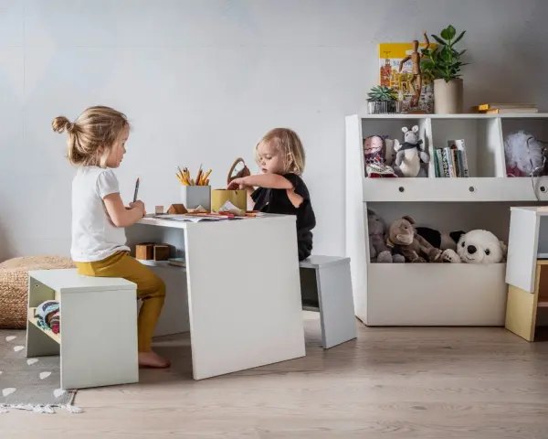 Dwie dziewczynki bawią się przy stoliku, tworząc przytulny kącik zabaw dla dziecka w salonie. Na półkach stoją pluszaki i książki.