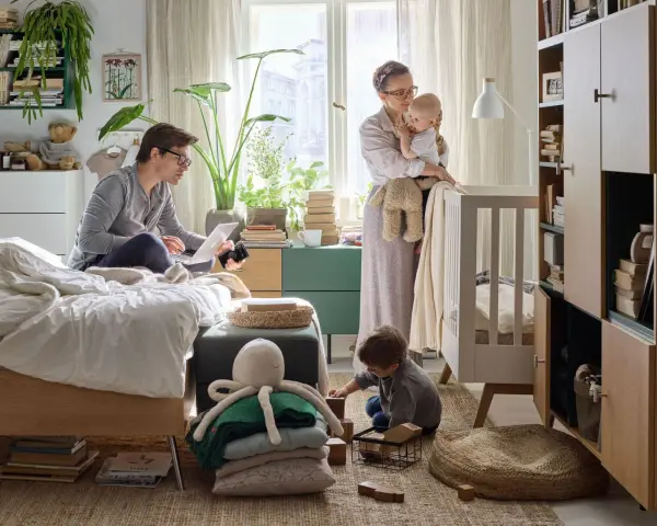 Wspólny pokój rodziców z dzieckiem. Ojciec pracuje przy laptopie, matka tuli niemowlę, starsze dziecko bawi się klockami.