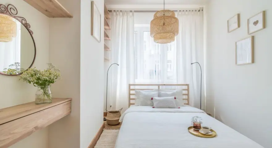 Mała sypialnia inspiracje: jasne wnętrze z drewnianym łóżkiem, wiklinową lampą i lustrem.