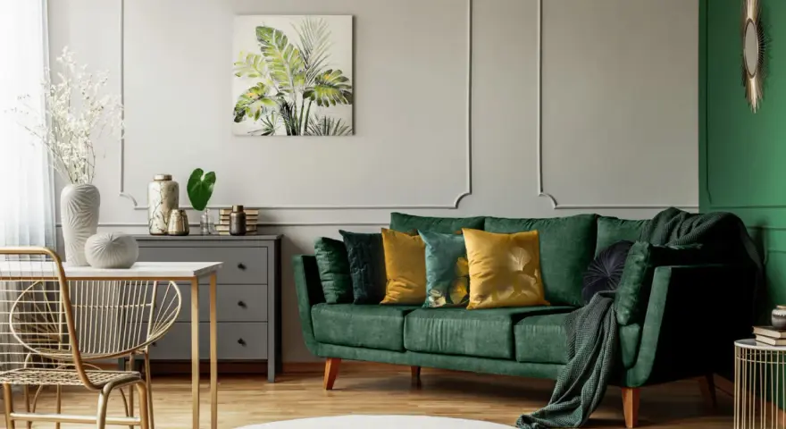 Jak rozjaśnić salon z ciemnymi meblami? Zielona sofa, złote akcenty i jasne dodatki dodają lekkości.