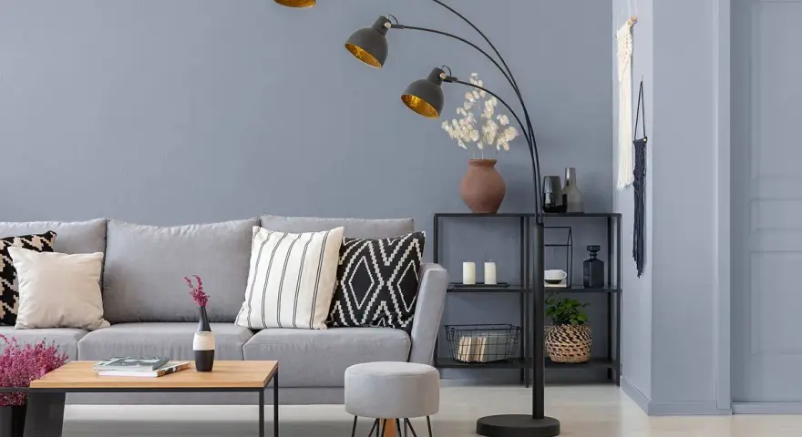 Nowoczesny salon z szarą kanapą i stolikiem. Lampę łukową w kolorze grafitowym oświetla złote wnętrze kloszy.
