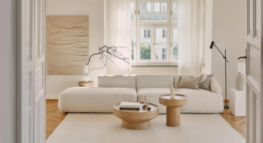 Jasny salon z sofą i stolikami kawowymi. Białe meble na białej ścianie tworzą minimalistyczną, spokojną przestrzeń.