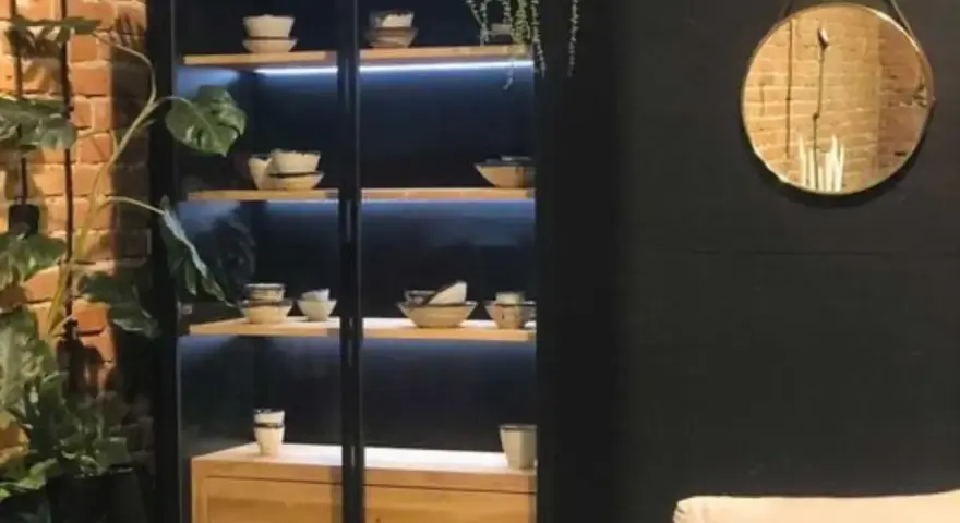 Elegancka witryna w salonie z podświetlanymi półkami, na których stoją misy i filiżanki. Idealna inspiracja, co wstawić do witryny w salonie.