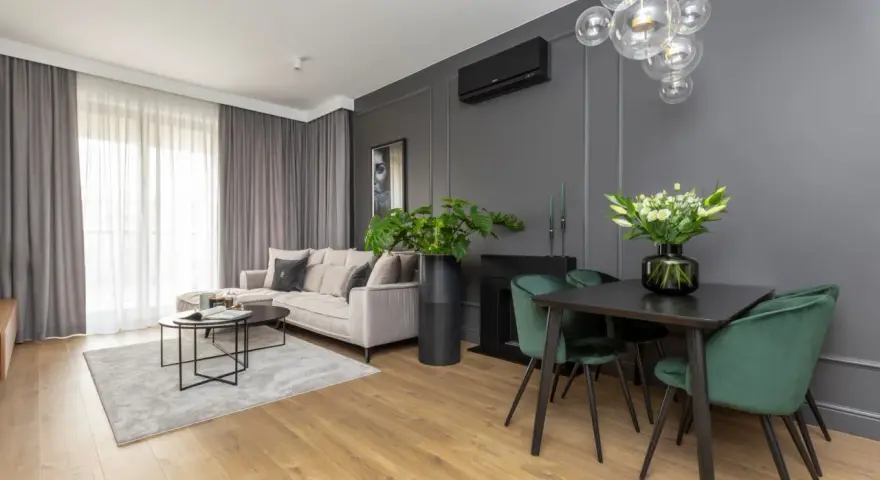 Nowoczesny salon z sofą w odcieniu beżu, dywanem w barwie szarej i zielonymi krzesłami przy czarnym stole.