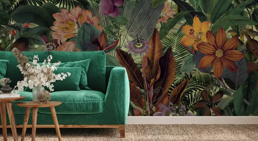 Aksamitna sofa w odcieniach zieleni, obok niej drewniane stoliki z bukietem. W tle bujna, tropikalna tapeta z kwiatami i liśćmi.
