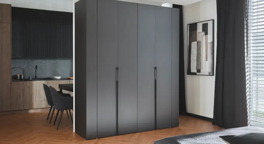 Nowoczesne oddzielenie kuchni od salonu za pomocą minimalistycznej zabudowy. W tle widać kuchnię z drewnianymi frontami i czarnym blatem.