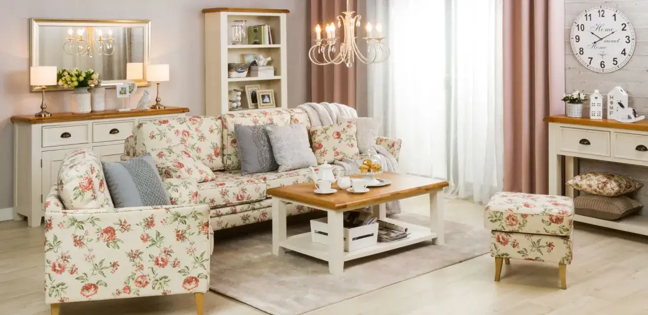 Przytulny salon w stylu shabby chic z kwiecistą sofą, fotelem i pufą. Drewniany stolik kawowy z ciasteczkami i filiżankami.