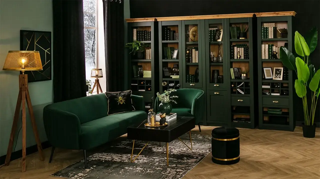Elegancka biblioteczka w salonie, pełna książek i dekoracji, obok zielonej kanapy i fotela.