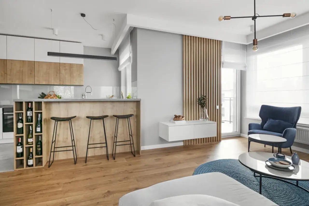 Nowoczesny szary salon inspiracje: kuchnia z wyspą, drewniane akcenty, wygodny fotel i stolik kawowy.