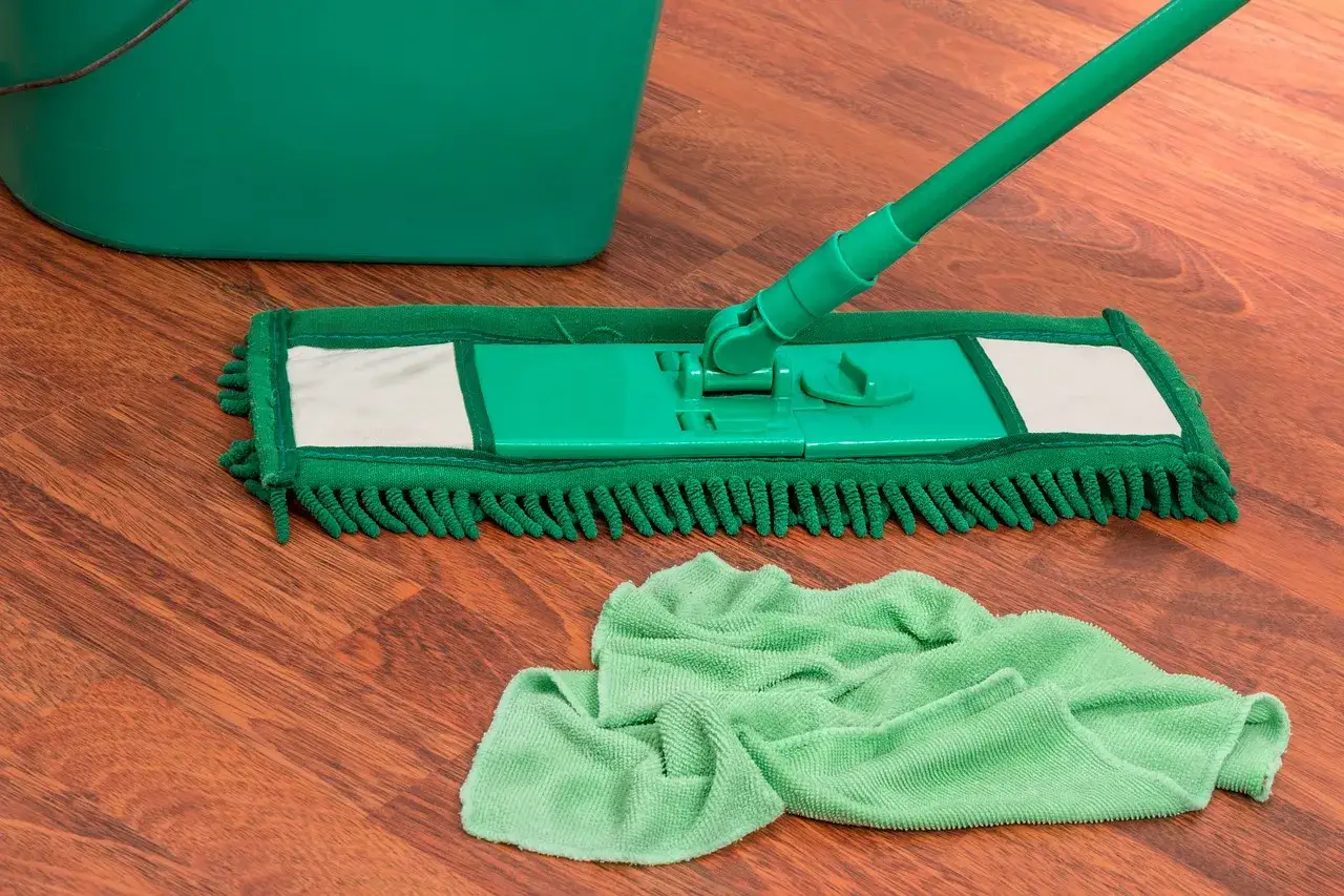 Zielony mop i ściereczka na drewnianej podłodze. Dowiedz się, czym myć panele, żeby nie było smug.