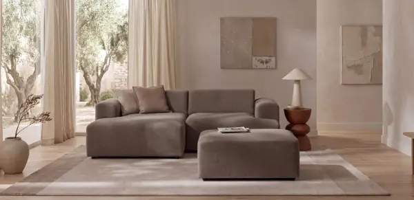 Wygodna sofa i puf w kolorze greige jaki to kolor, idealnie komponują się z jasnym wnętrzem i widokiem na drzewa.